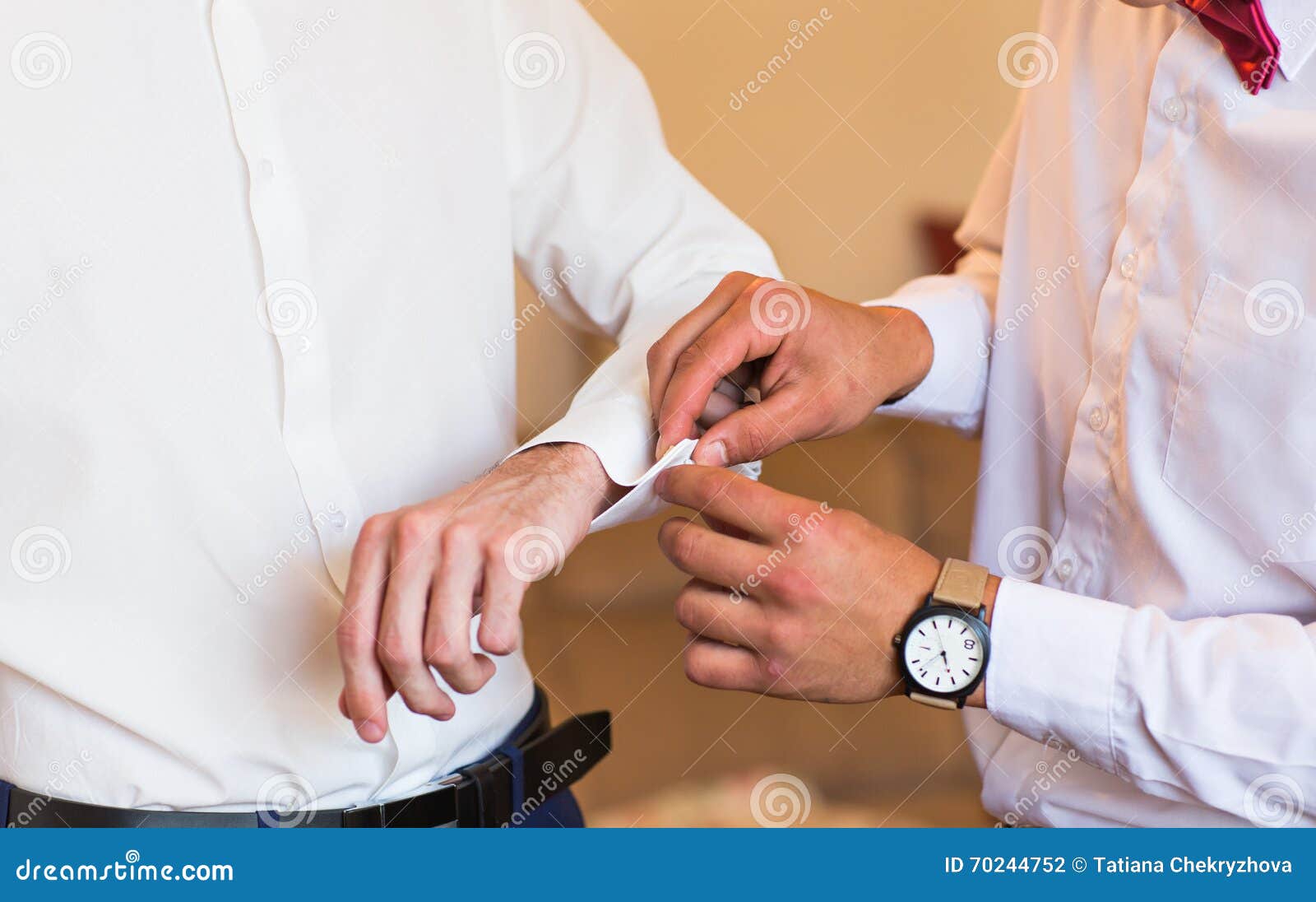 Novio de las ayudas del padrino de boda para poner el primer de las mancuernas. El padrino de boda ayuda a preparar para poner mancuernas