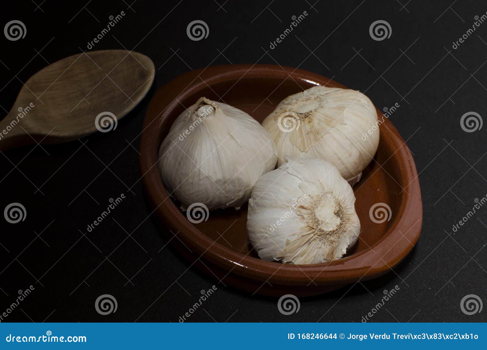 three garlic in clay pot with wooden spoon