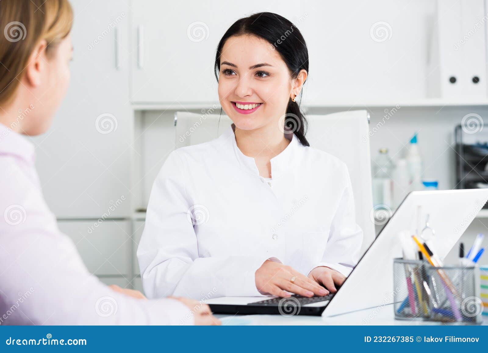 Nurse making appointment for client. Young female nurse makes appointment for visitor at reception