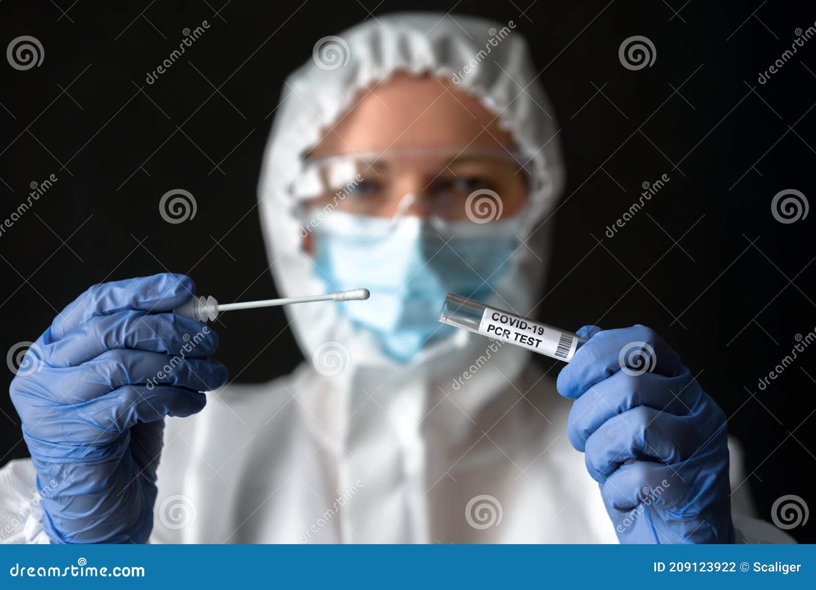 nurse in medical ppe suit holds tube of coronavirus pcr test