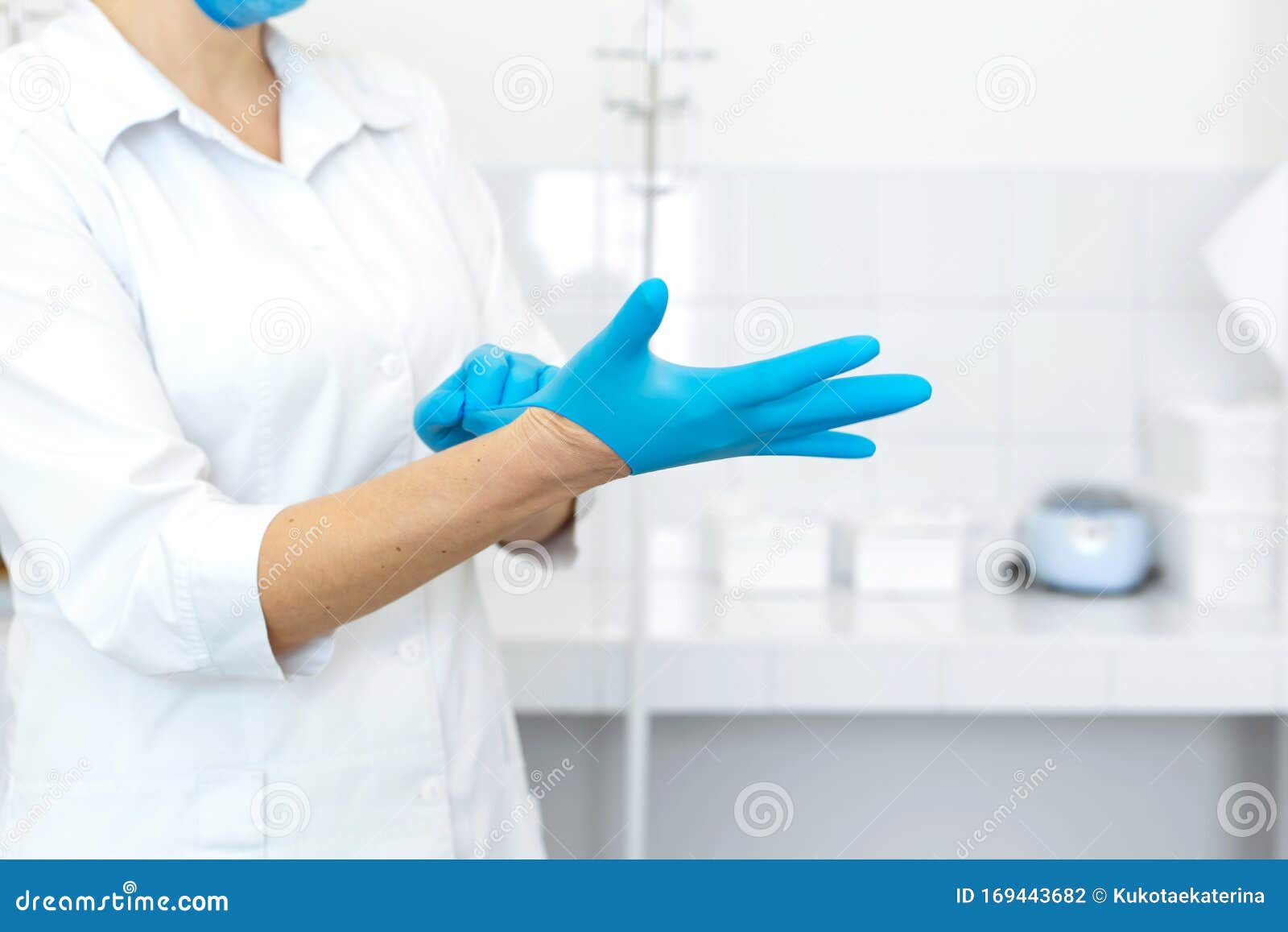 a nurse in a white coat puts on rubber gloves before a medical procedure in a bright handling room