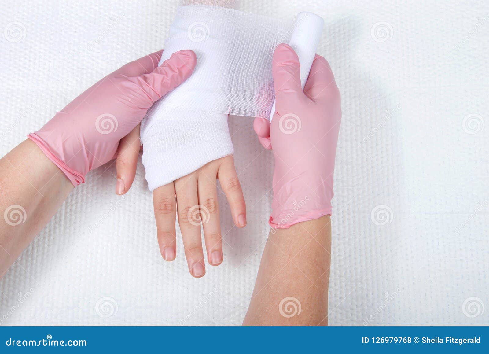 Nutra com as luvas cor-de-rosa que envolvem a mão das moças com molho da gaze. Mãos fêmeas novas que vestem as luvas cor-de-rosa que envolvem a gaze no tratamento médico novo da mão e do pulso