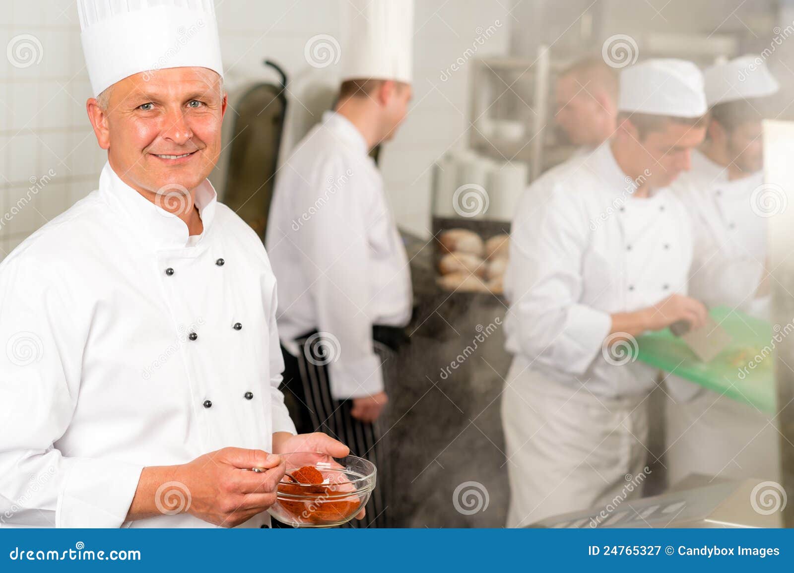 O cozinheiro chefe de sorriso da cozinha profissional adiciona o alimento da especiaria