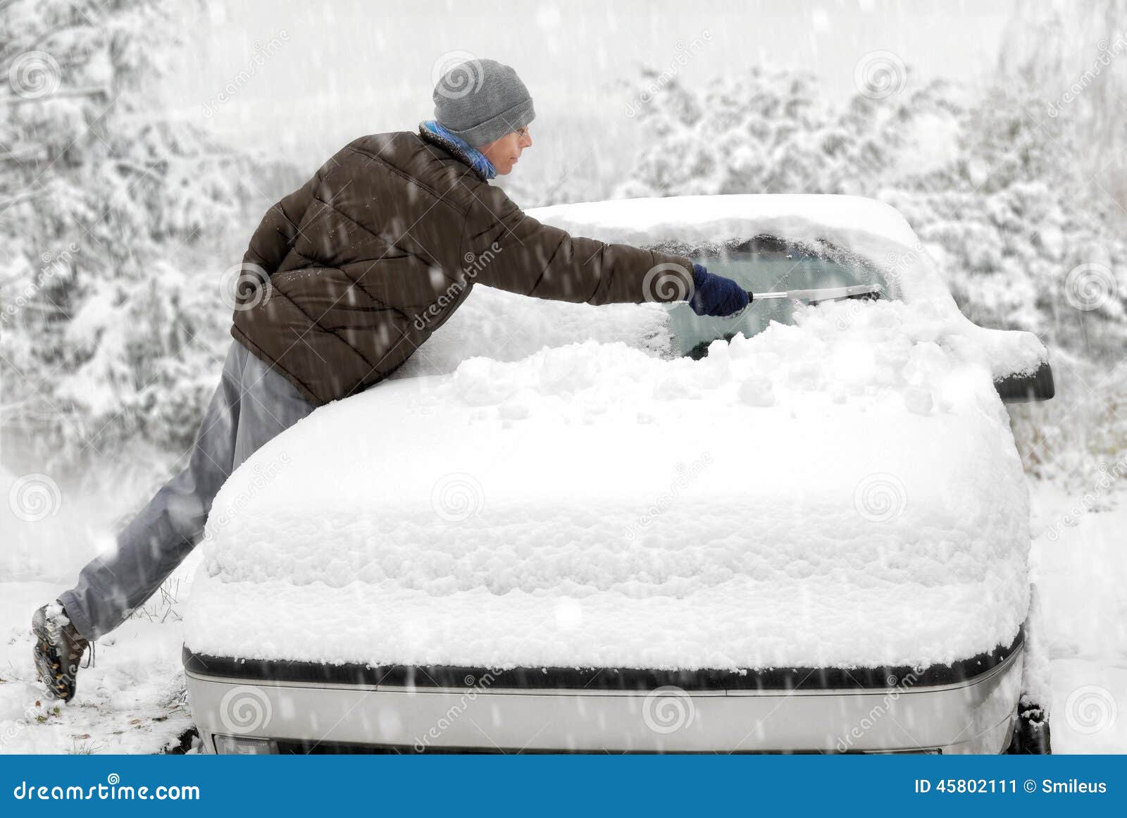 O homem escova a neve fora de seu carro. Homem novo que escova a neve fora de seu carro em um dia de inverno frio na queda de neve