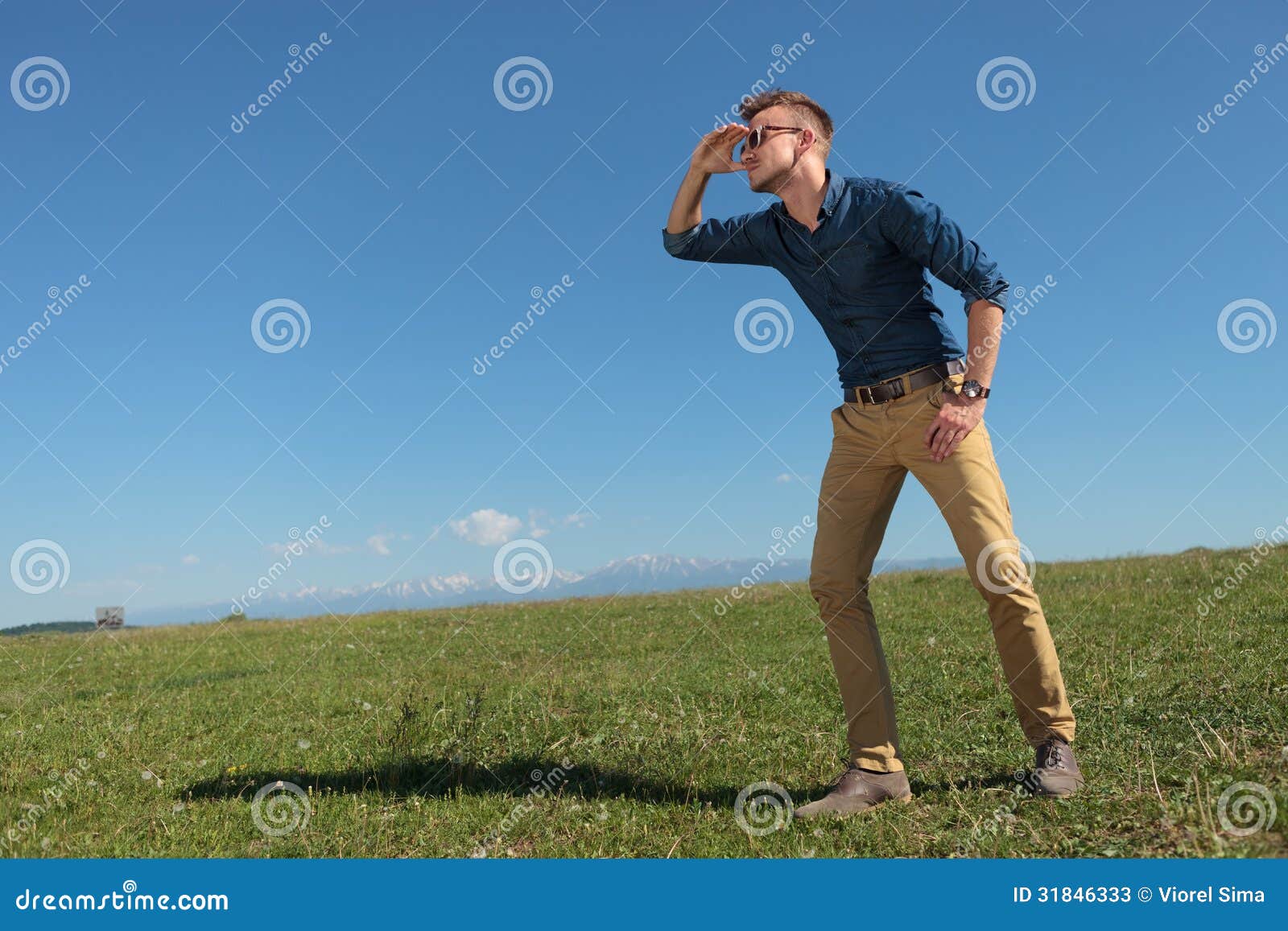 O homem ocasional olha longe. Vista exterior ocasional do homem novo longe com mão acima dos olhos