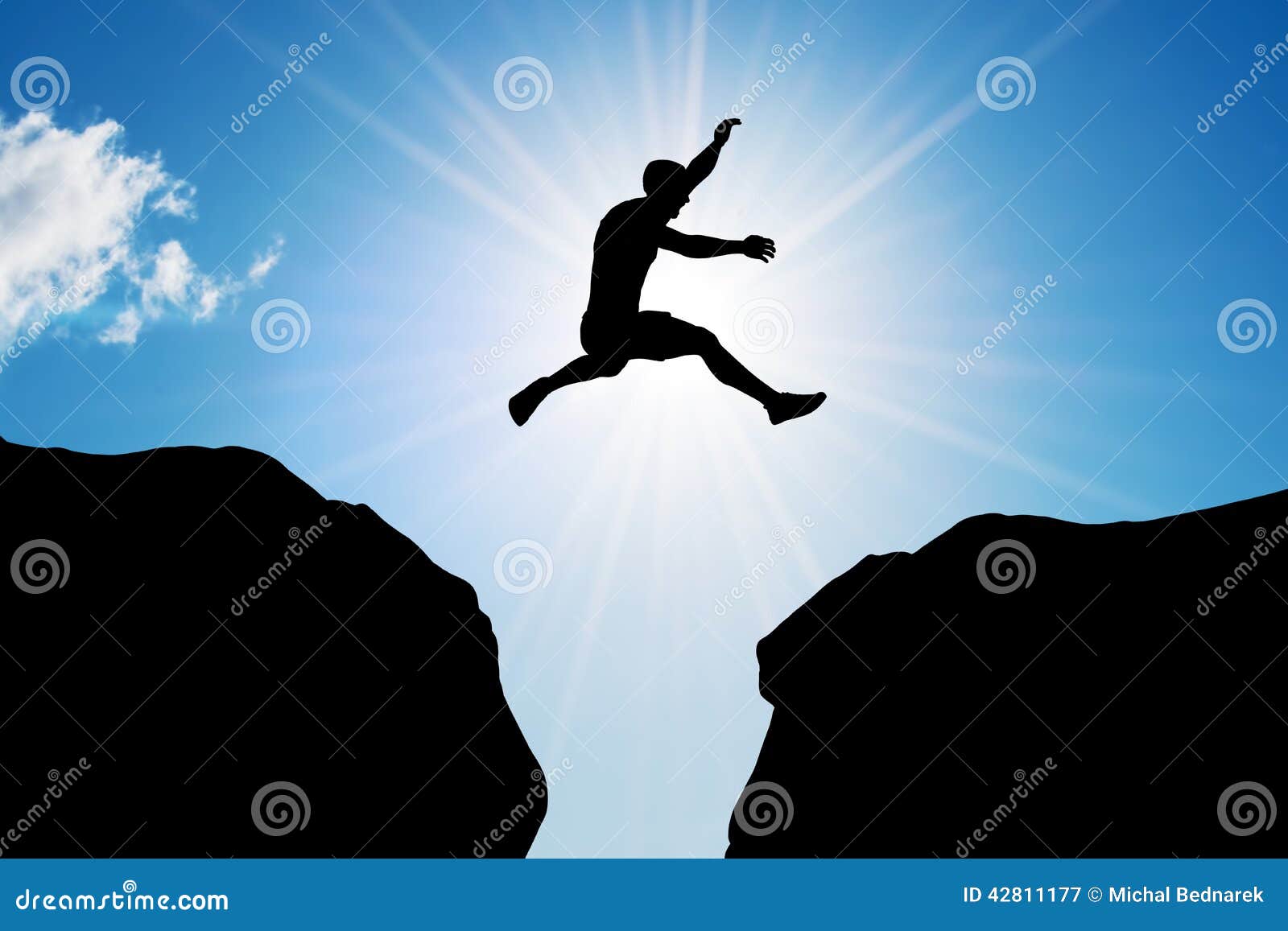 O homem que salta sobre o precipício Risco, desafio, sucesso. Equipe o salto sobre um precipício entre duas montanhas rochosas na luz do sol Liberdade, risco, desafio, sucesso