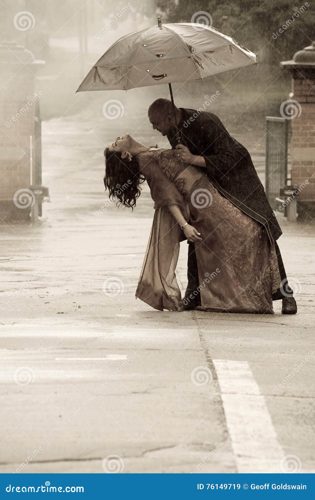 O indiano vestiu espertamente a dança dos pares sob um guarda-chuva na chuva. O indiano vestiu espertamente os pares que guardam um guarda-chuva na chuva