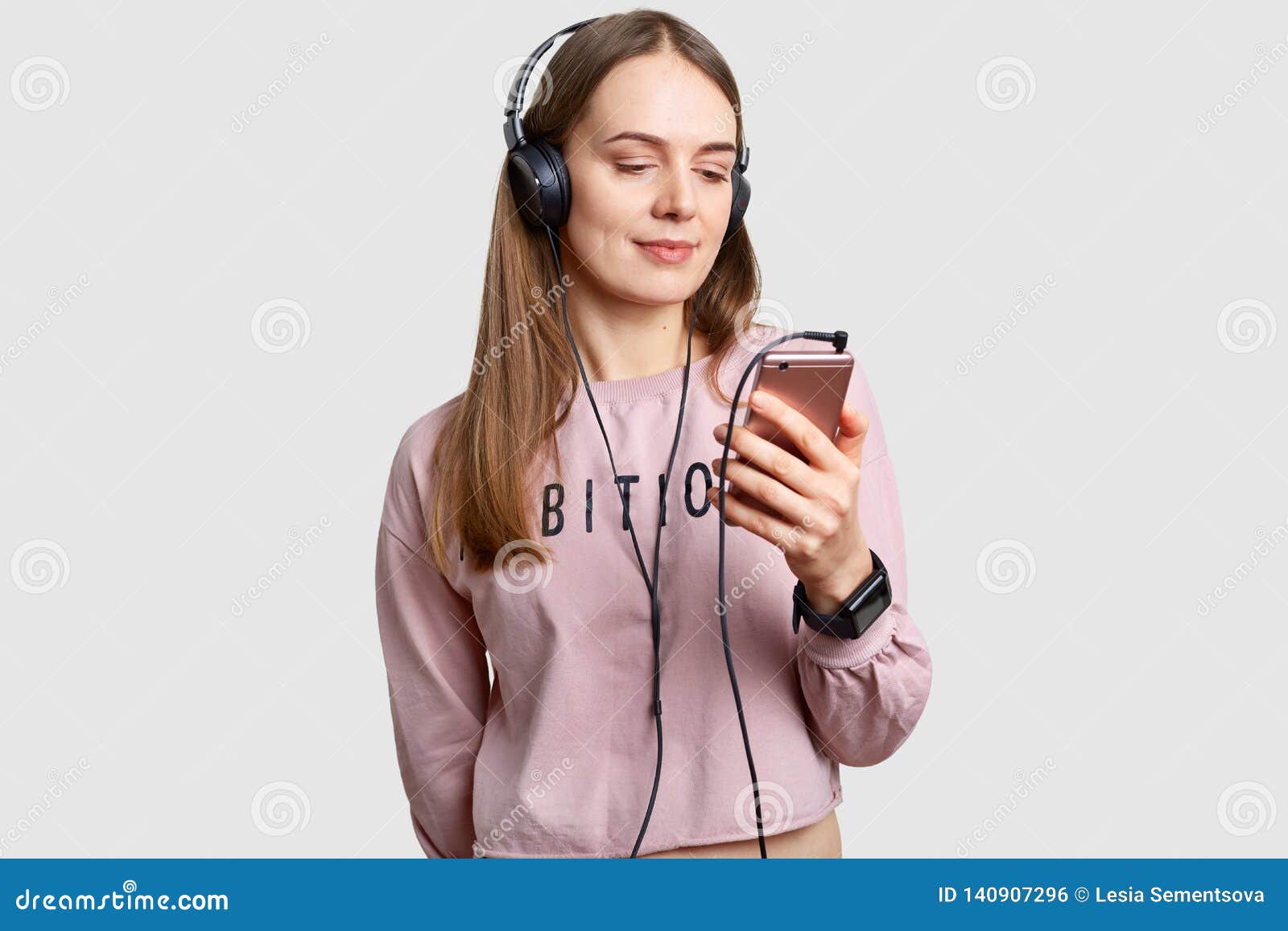 O tiro interno do adolescente focalizado na tela do telefone esperto, escuta música com os fones de ouvido da lista de músicas, aprecia o som puro alto, tem o cabelo longo, isolado sobre o fundo branco Conceito do lazer