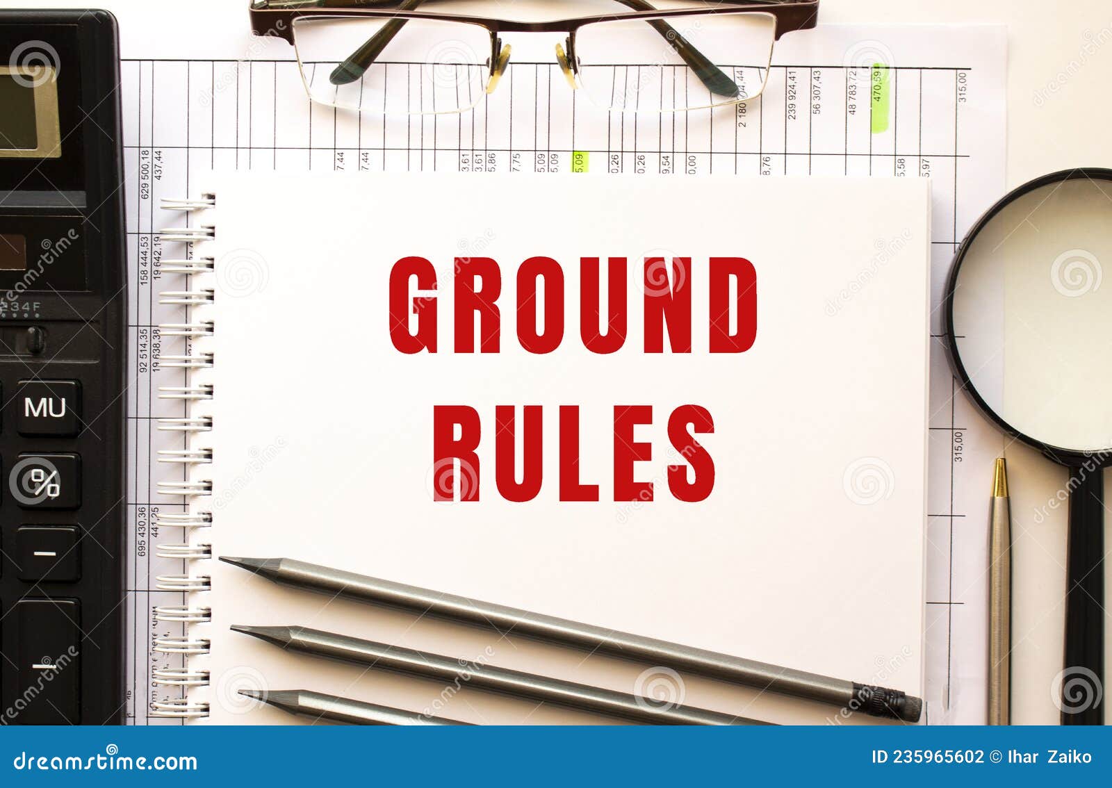 office desk with financial papers, calculator, glasses. notepad with the text ground rules.