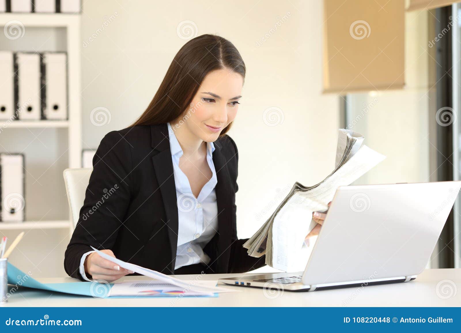 Office Worker Comparing Online Content with a Newspaper Stock Photo