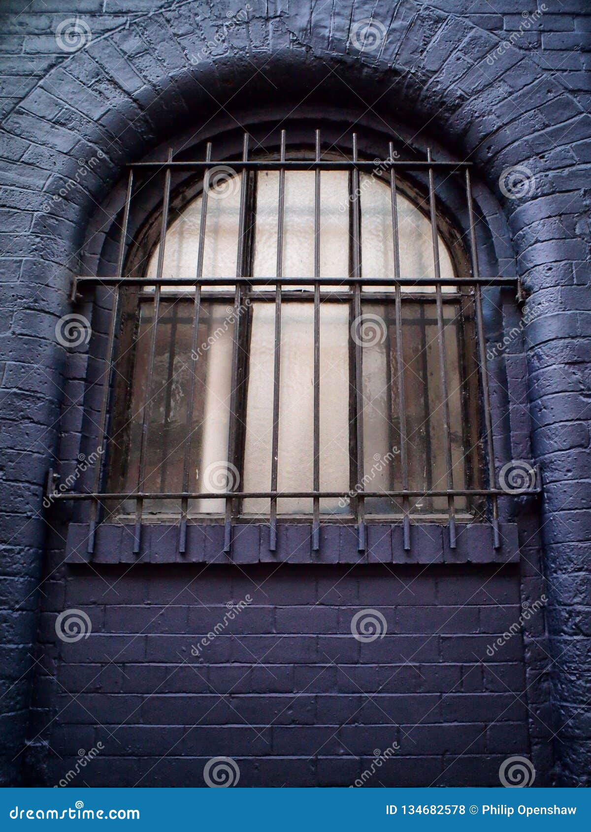 Old Arched Window in a Black Brick Wall with Heavy Metal Bars Stock