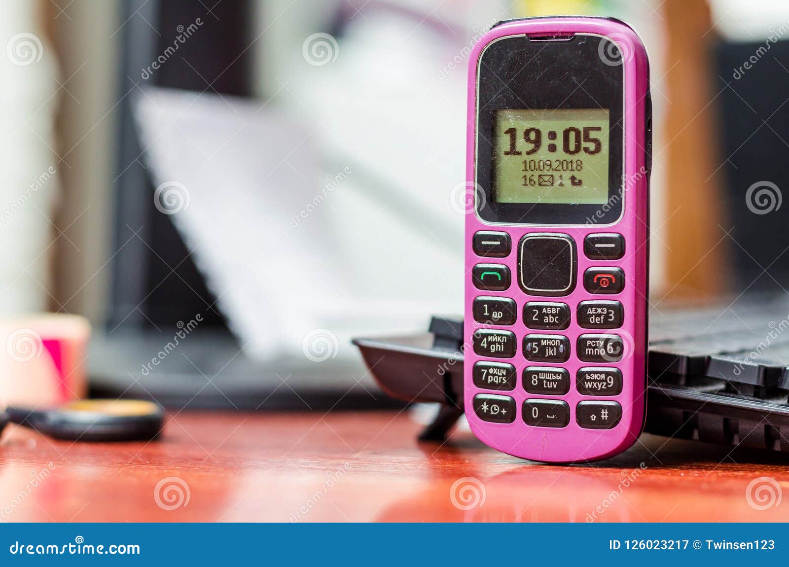 old button mobile phone pink color on the desk near a computer k
