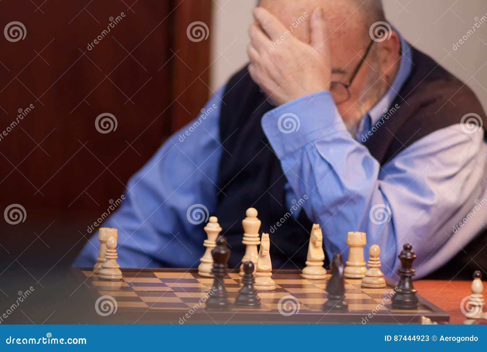 Old man in checked shirt holding glasses and thinking about next chess move  in game with imaginary opponent Stock Photo