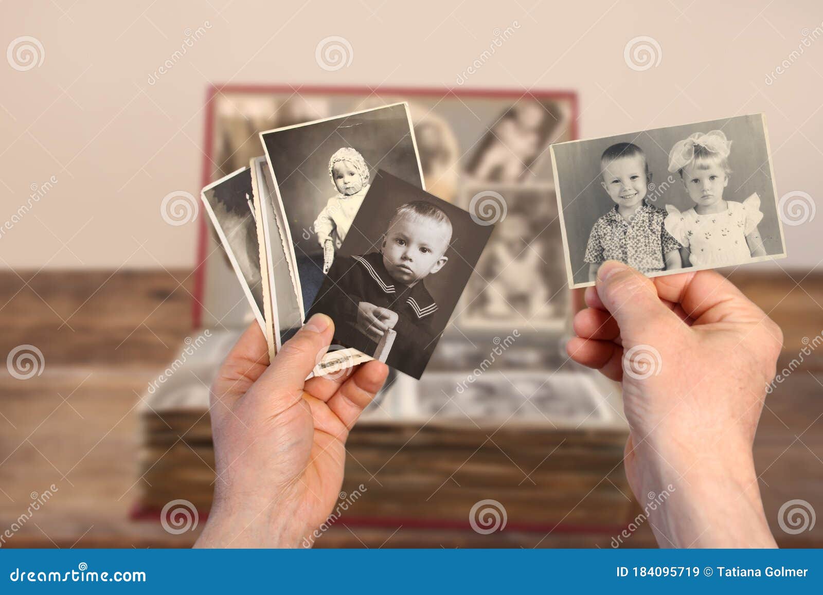 old manÃ¢â¬â¢s male hands hold old retro family photos over an album with vintage monochrome photographs in sepia color and wooden