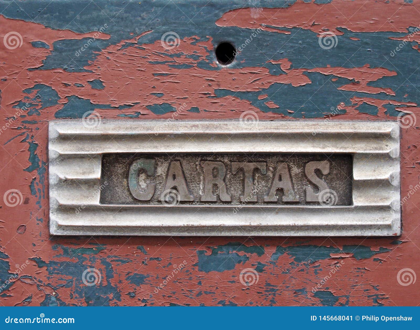 old metal letterbox in a red wooden door with chipped peeling paint with the word cartas, translation from portuguese is mail