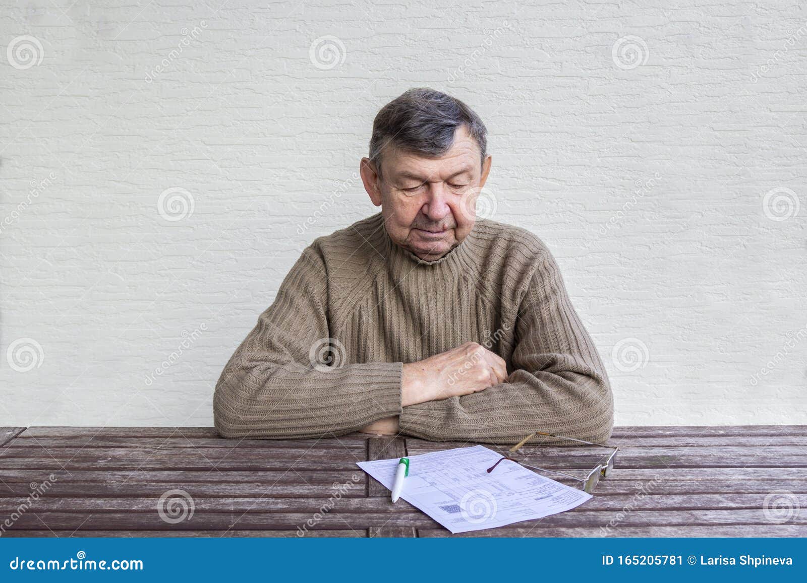 portrait of elderly man sitting at table with white sheet of paper, pen and glasses