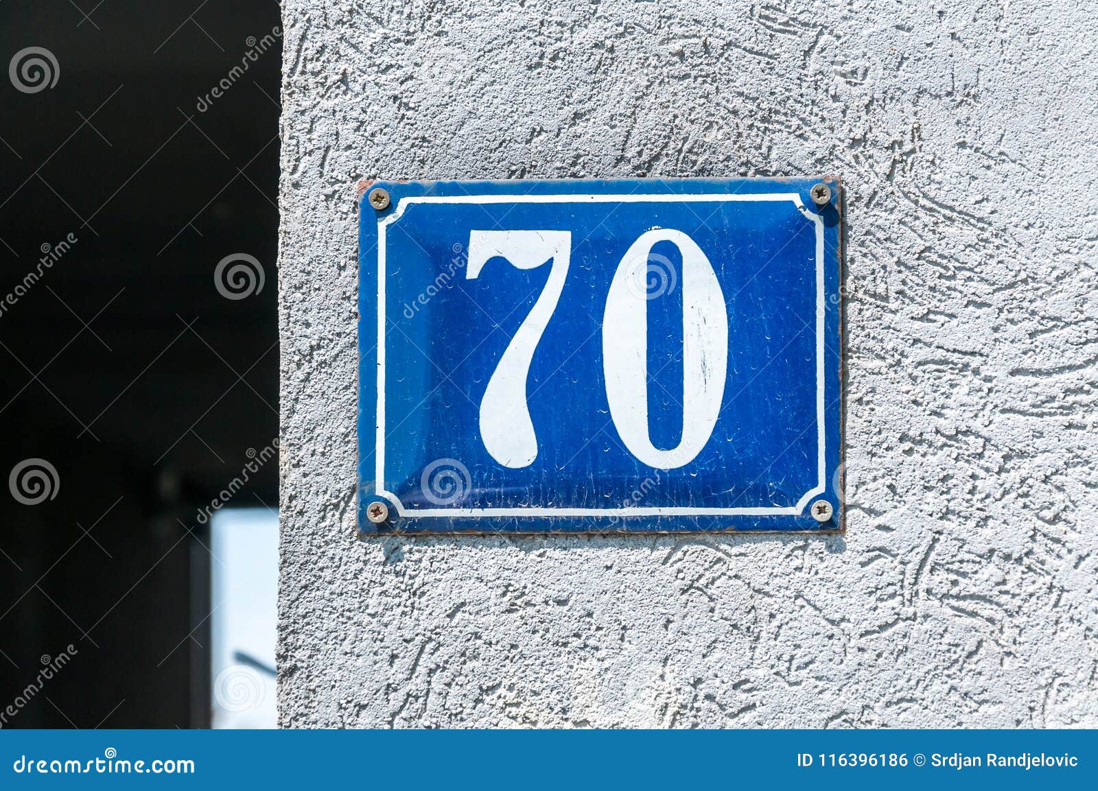old vintage house address metal number 70 seventy on the plaster facade of abandoned home exterior wall on the street side