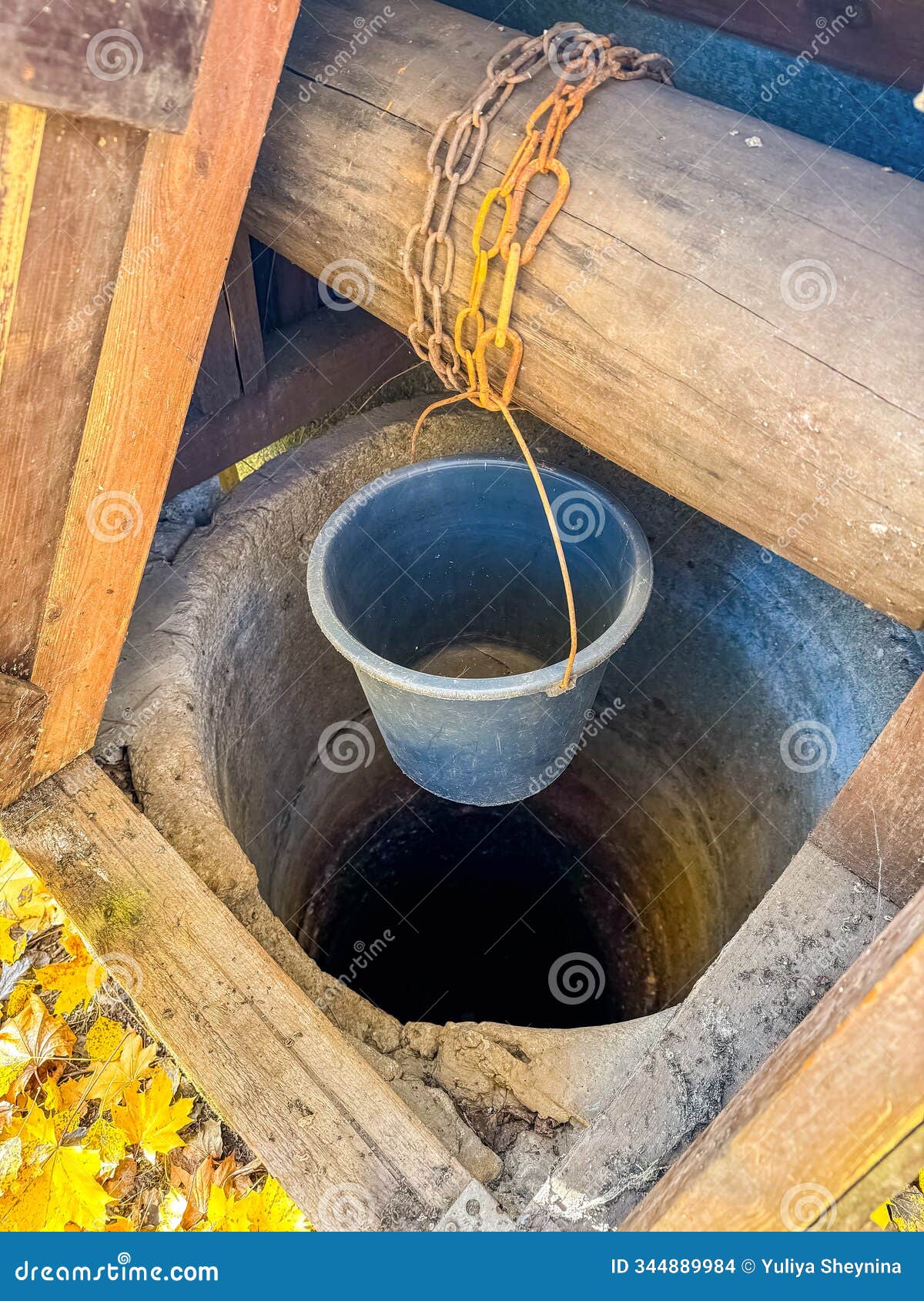 old wooden water well with rusted chain and hanging bucket in autumn setting