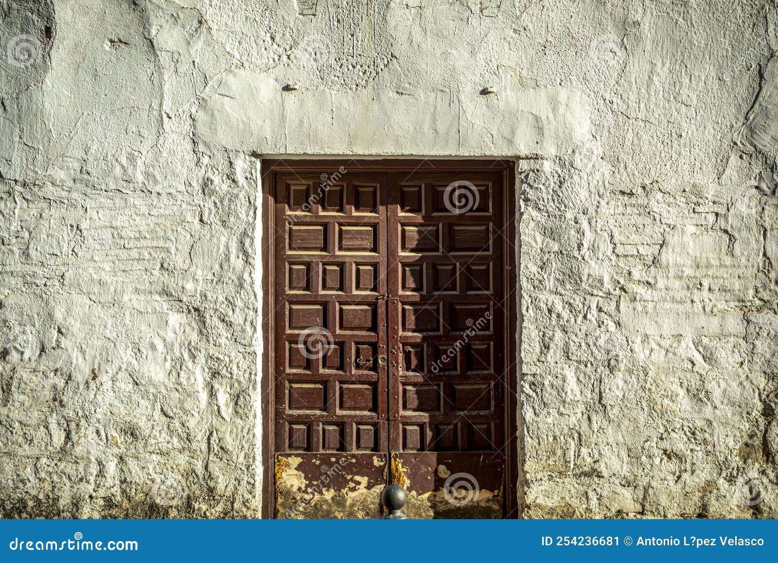 old and worn maroon double wooden door with a lock on a whitewashed wall very textured