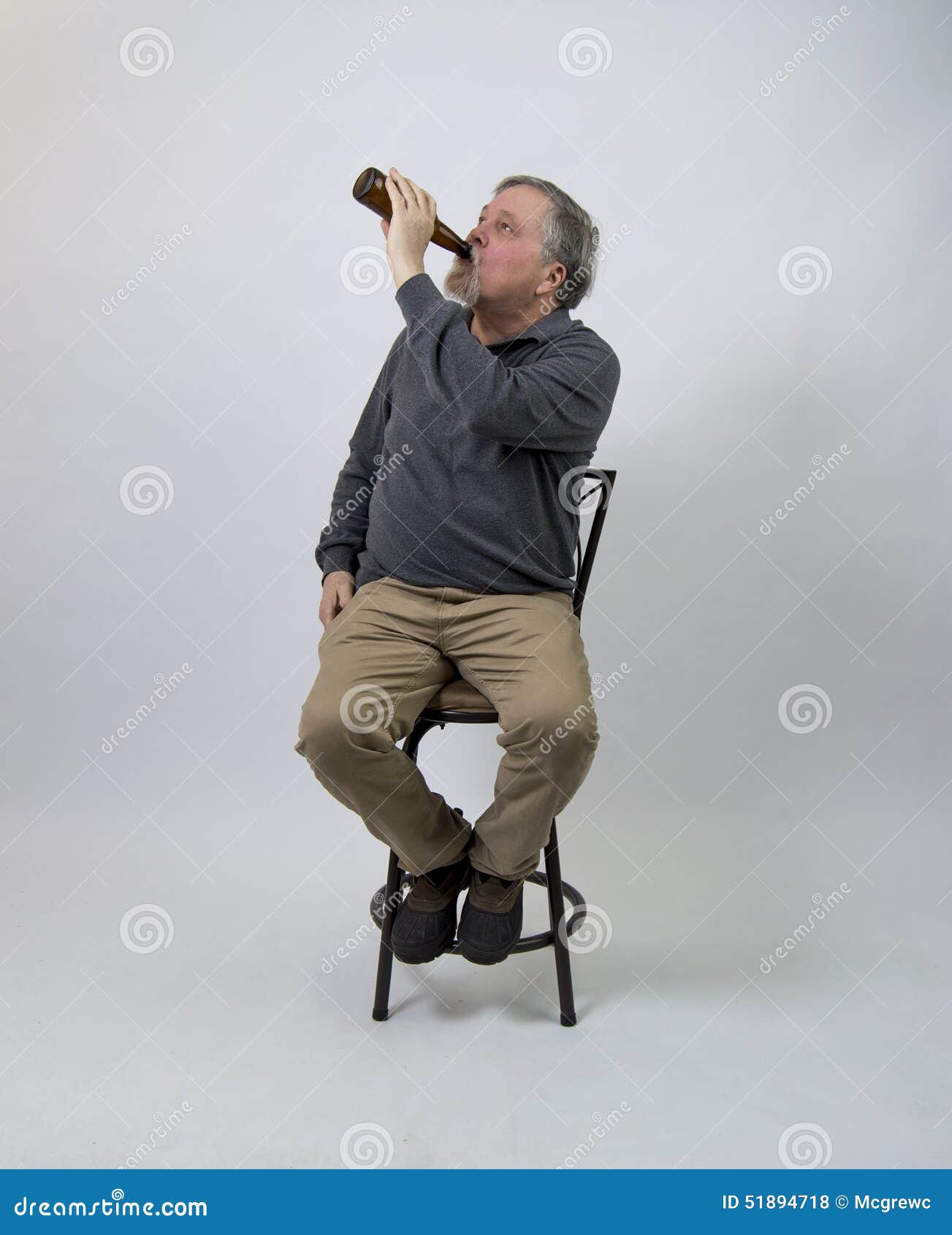 Older Man Sitting on Stool Drinking Beer from Bottle Stock Photo