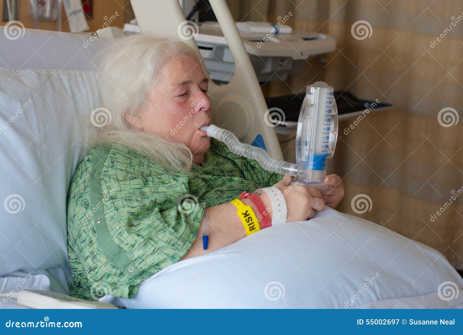 older woman in hospital bed using incentive spirometer
