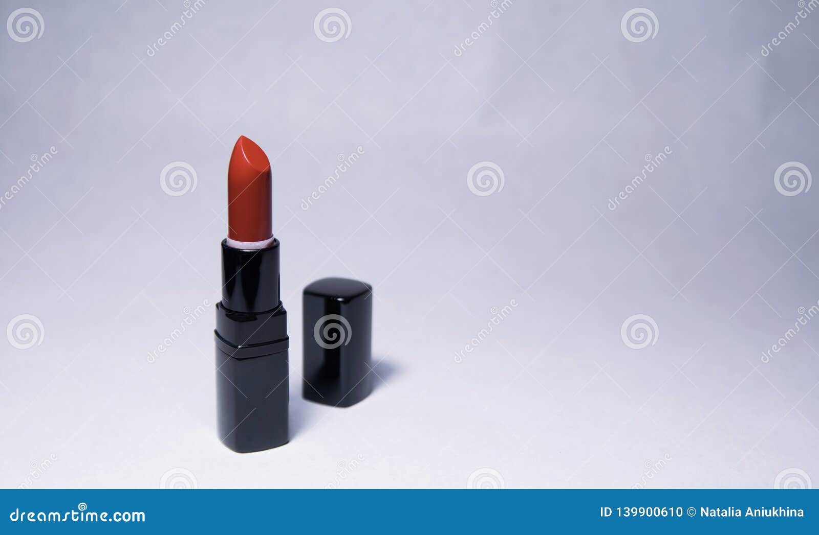 carrot-colored lipstick stands vertically open with a black cap near in the center on a white background
