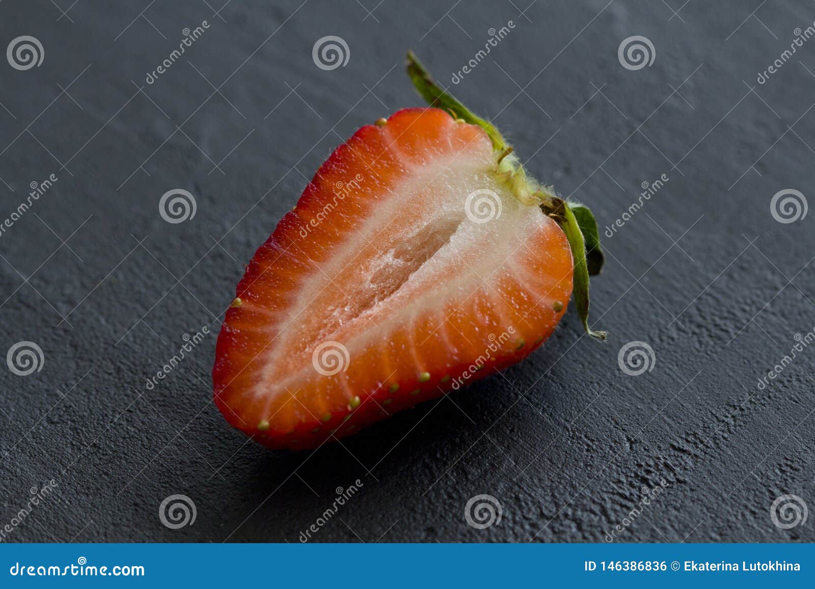 one half of strawberry, cut red beautiful strawberry close-up, on a black dark concrete background. macro shooting. fruit erotica