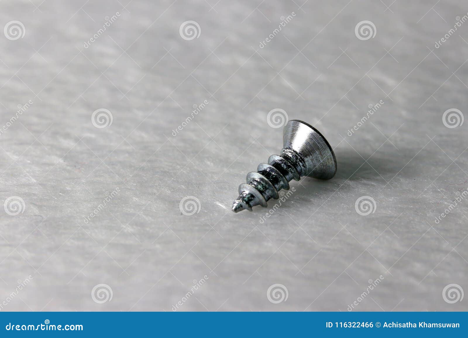 one metal put on the white fabric floor. it is a short, slender, sharp-pointed metal pin.