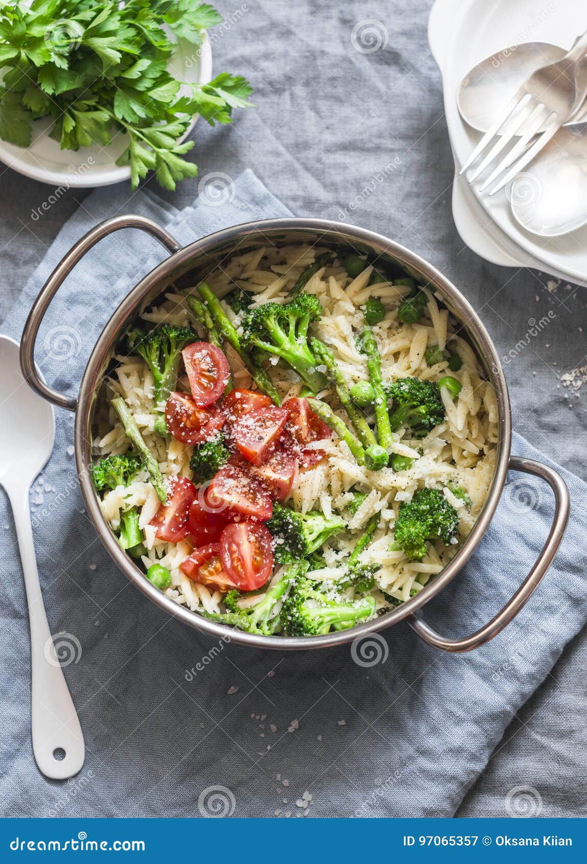 one pot orzo primavera. orzo pasta with asparagus, broccoli, green peas and cream in a saucepan. on a light background