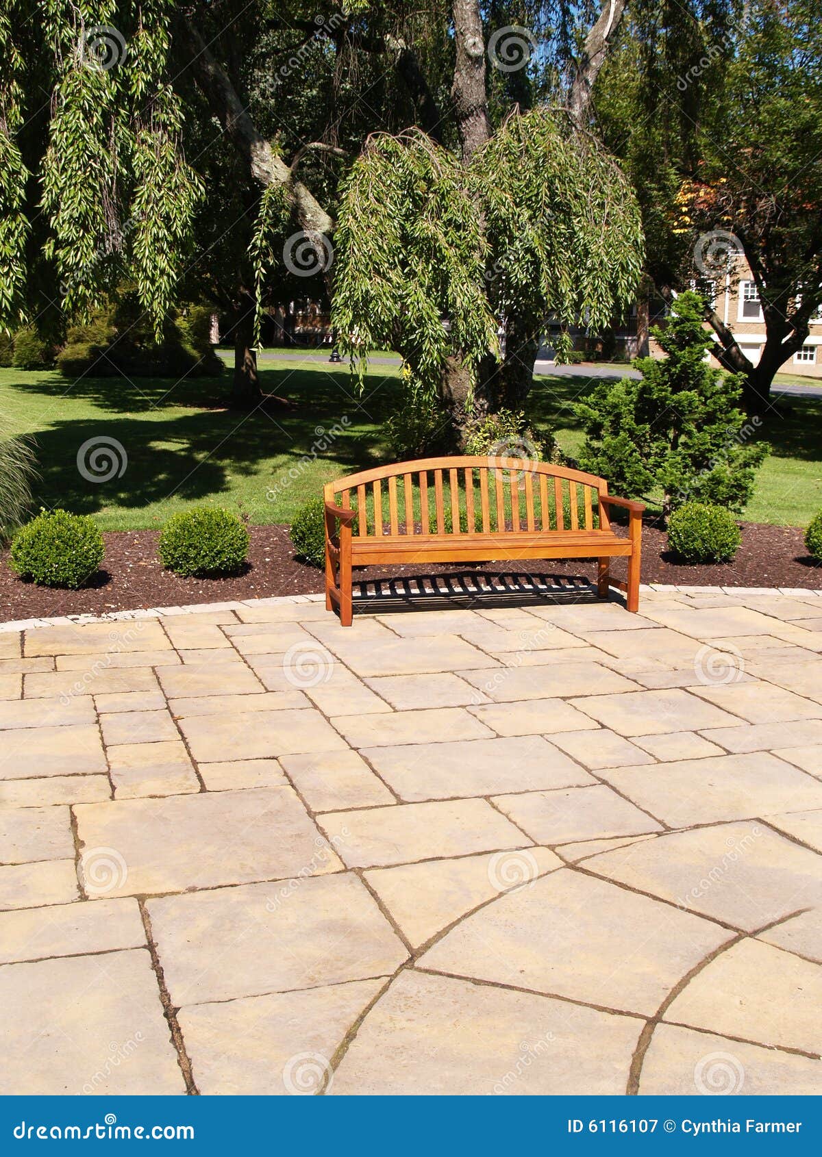 One wood bench. One empty wood bench by a stone patio