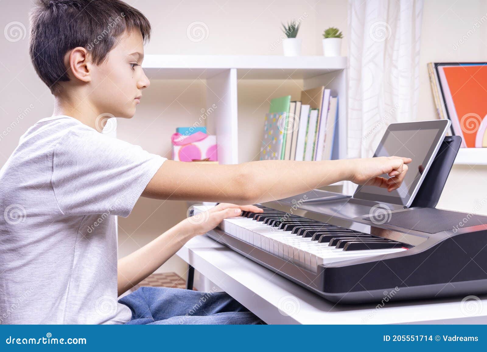 Foto de Young pianist boy looking at the digital tablet screen for learning piano  online at home. Music distance learning concept. do Stock