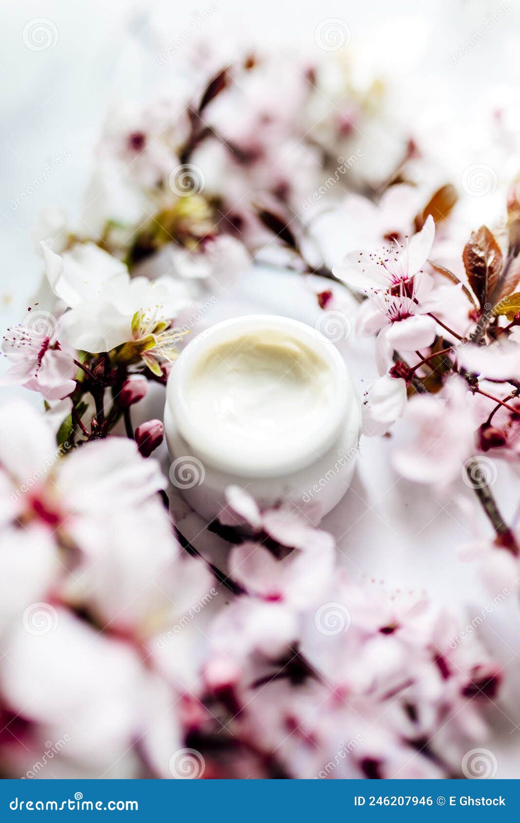 op view of cosmetic cream with pink cherry flowers in a blue glass jar. hygienic skincare lotion product.idioma de palabras