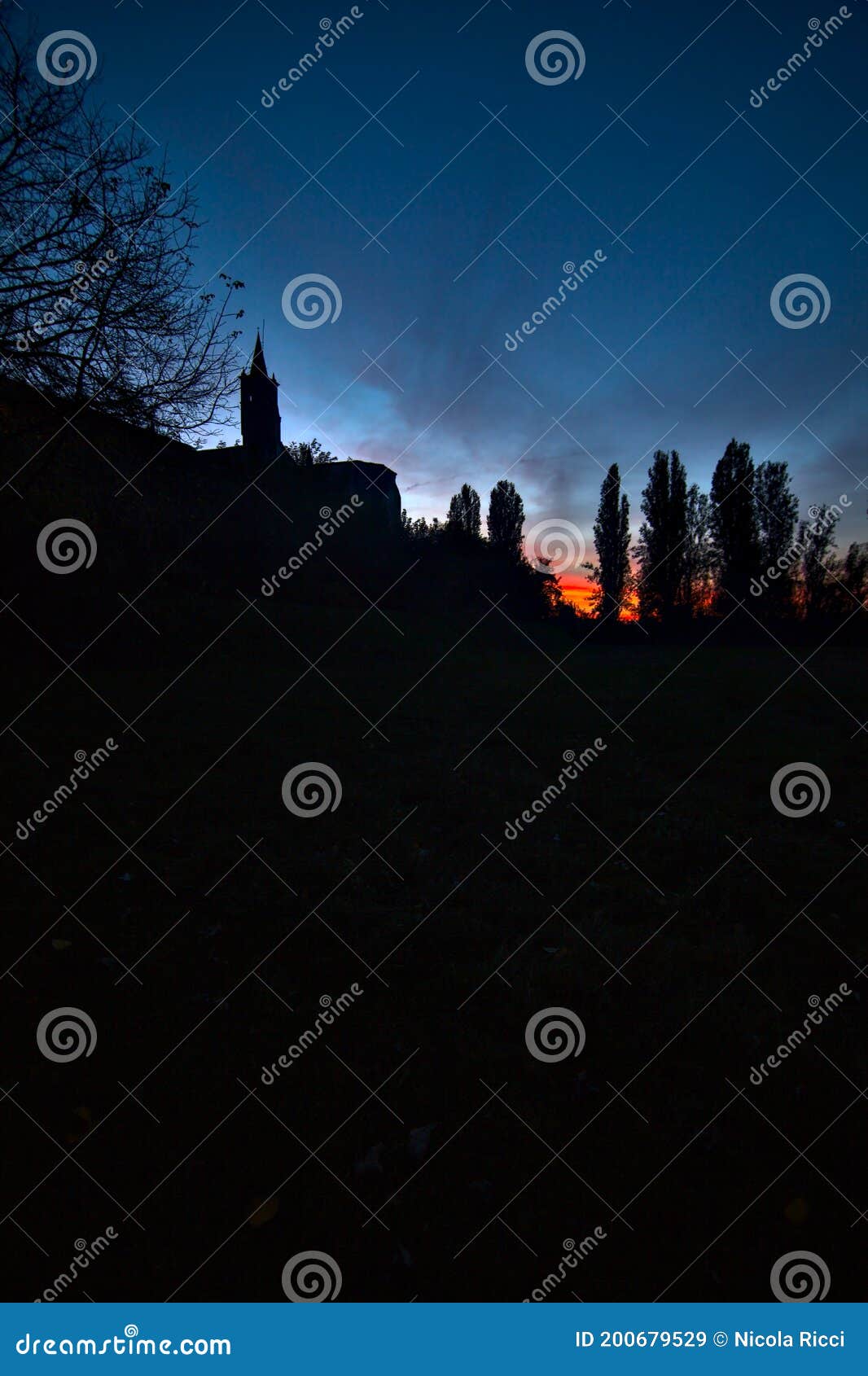 open field behind a church borderd by cypresses at sunset in autumn