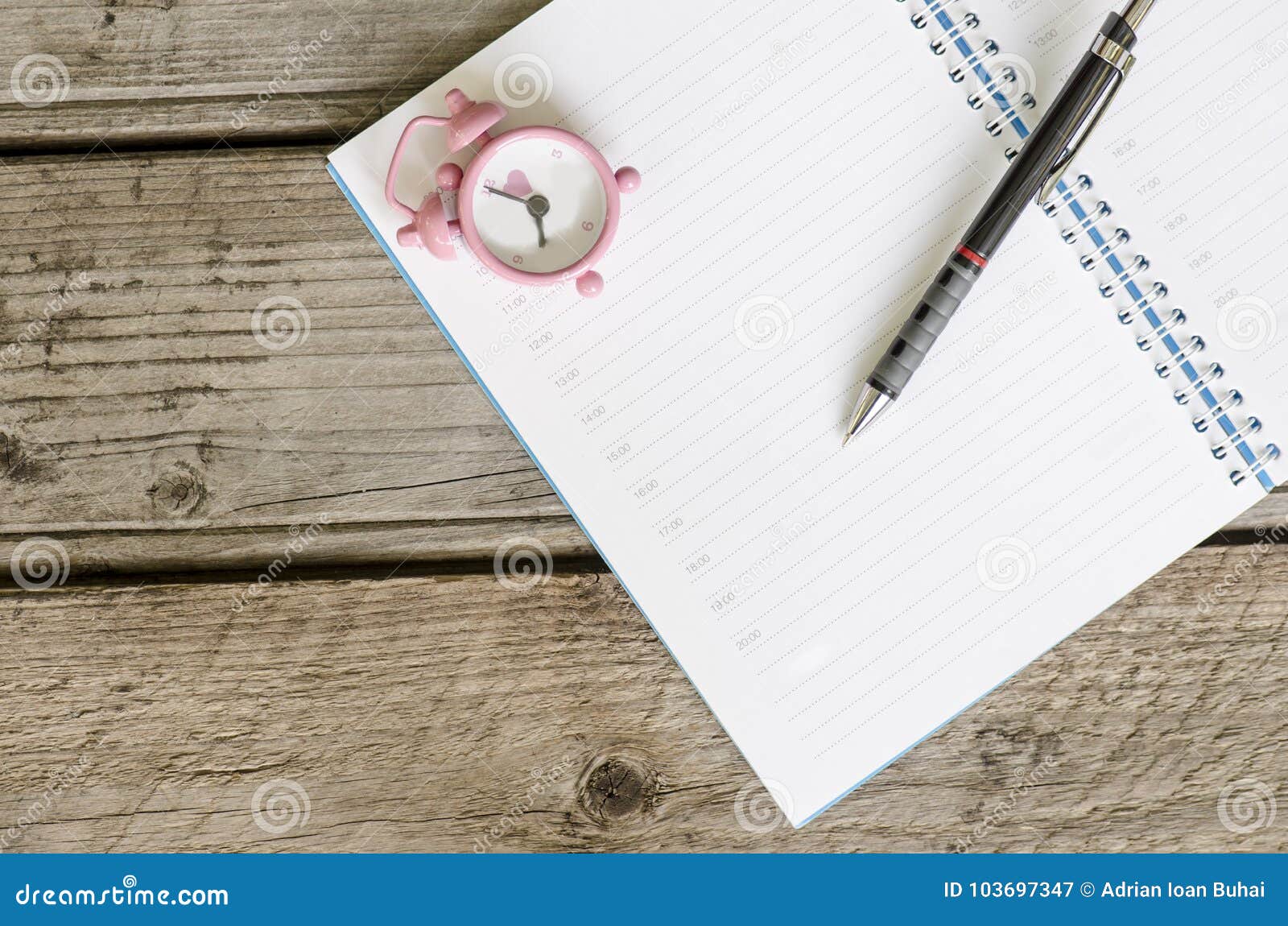 open notebook agenda with timetable and small pink clock at 8:00 am and pen on wooden background