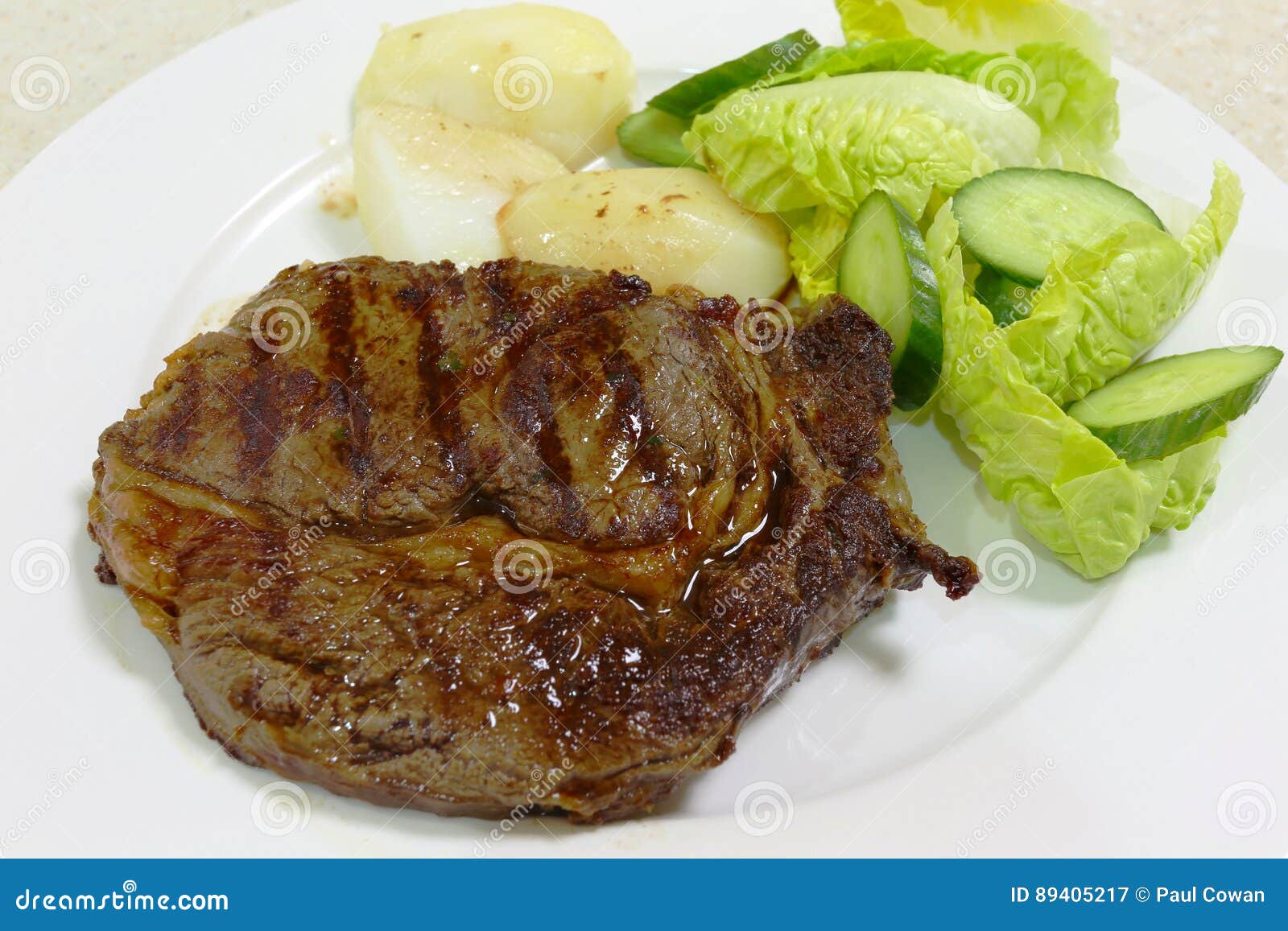 Opinião lateral do bife de Ribeye. Uma refeição do bife grelhado ou grelhado do ribeye serviu com batata fervida e uma salada verde