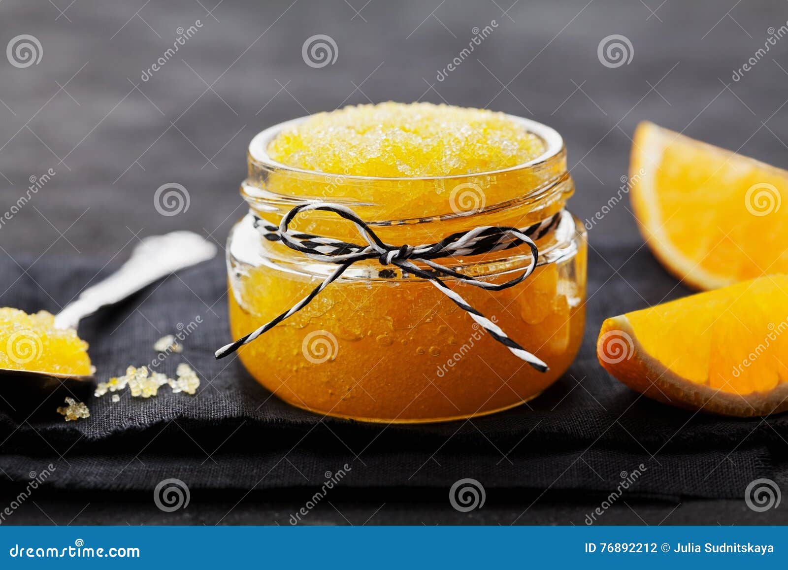 orange body scrub with sugar and coconut oil in glass jar on black table. homemade cosmetic for peeling and spa care