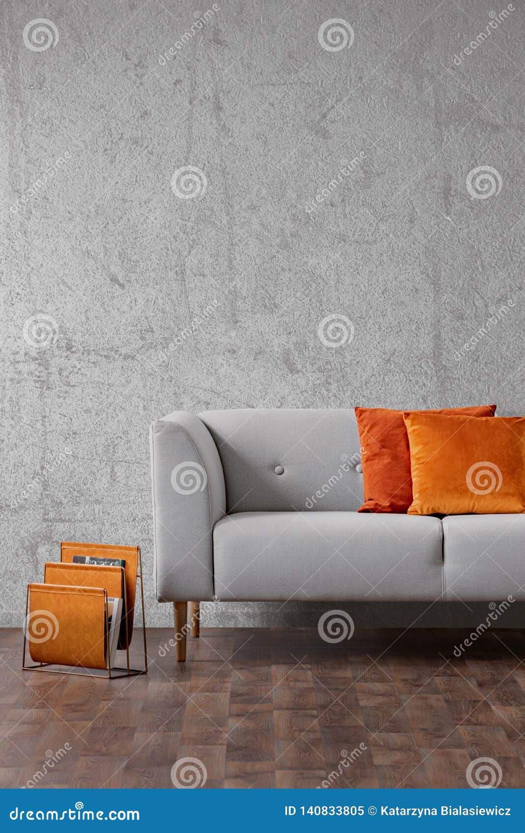 orange pillows on grey settee in living room interior with concrete wall and wooden floor. real photo