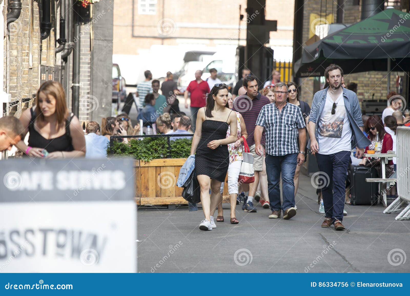 LONDRES, INGLATERRA - 12 de julho de 2016 os homens e a mulher do moderno vestiram-se no estilo fresco do londrino que andam na pista do tijolo, uma rua popular entre povos na moda novos