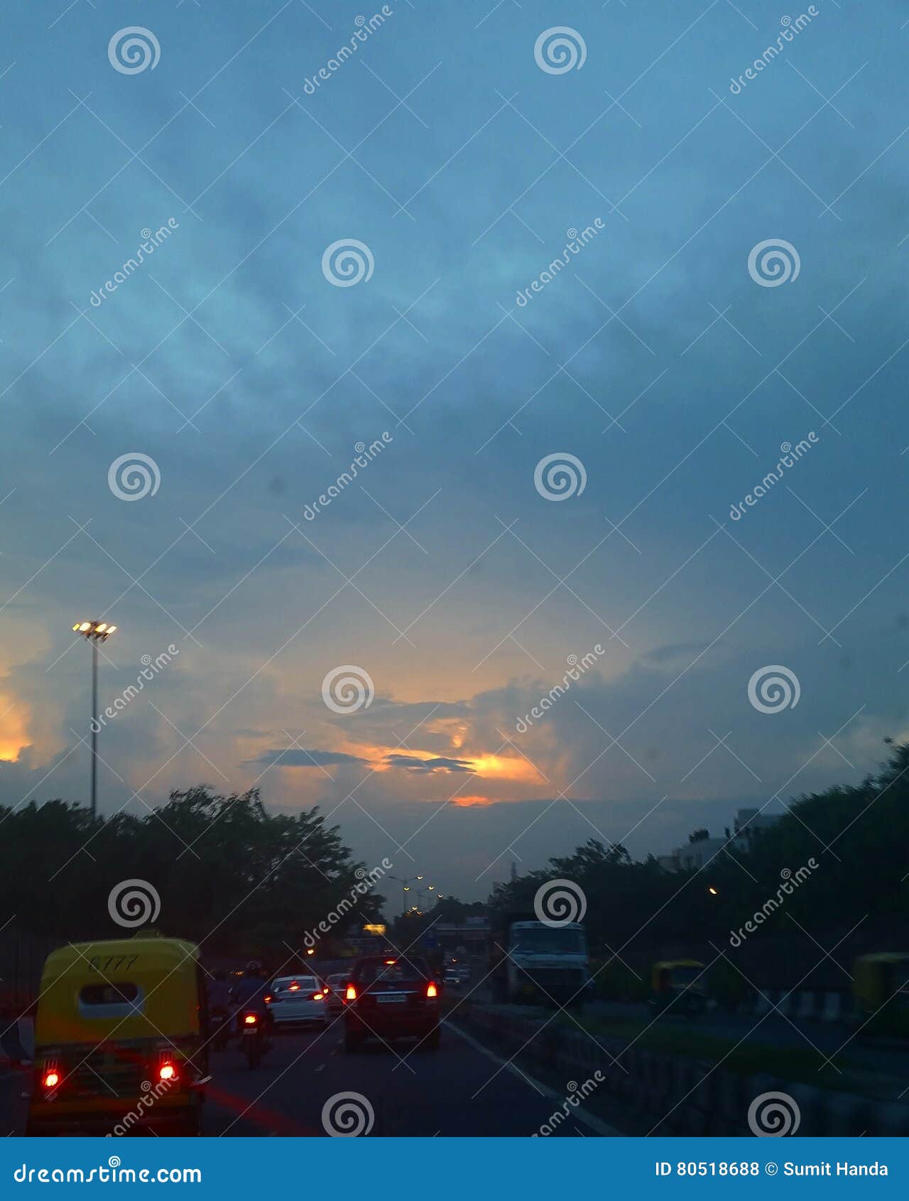 Oscuridad en la ciudad. Tráfico de la tarde en Delhi contra un horizonte de oscurecimiento con las pequeñas motas de la luz del sol todavía que filtran a través
