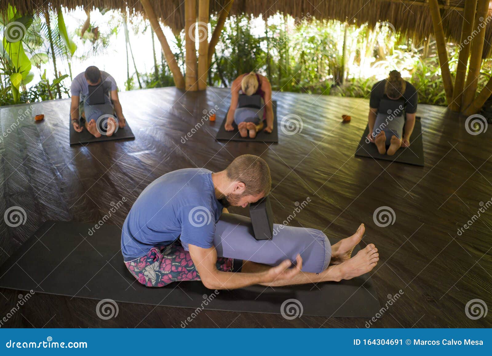 outdoors yoga lesson - group of young people and coach man practicing relaxation exercise at asian wellness retreat hut training