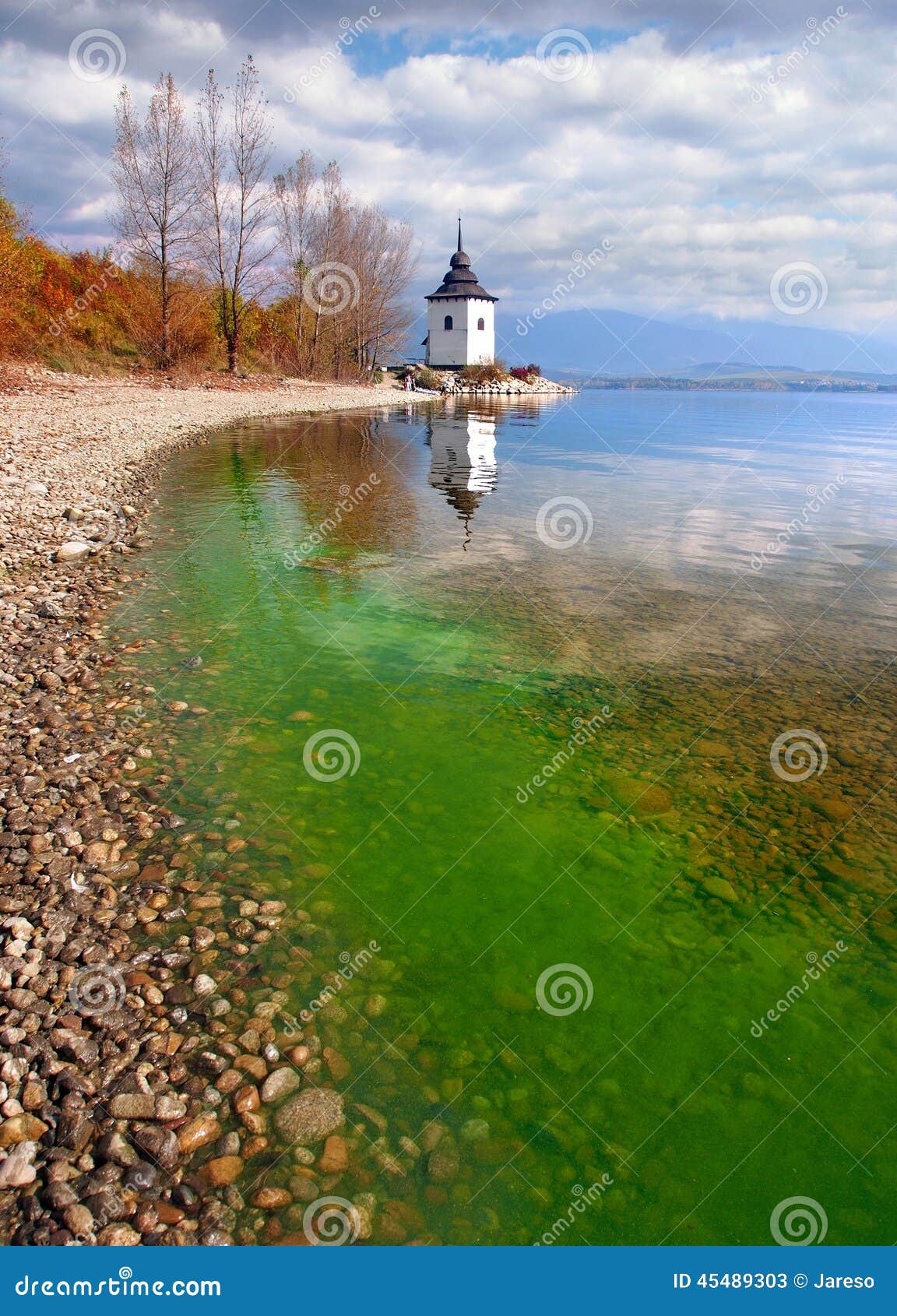 Outono no lago Liptovska Mara, Eslováquia. Uma opinião ensolarada do dia do outono que retrata a costa do lago Liptovska Mara, com as algas verdes na água e nas sobras da torre que pertenceram uma vez à igreja histórica da Virgem Maria Os montes de Tatras ocidental, montanhas de Rohace, podem ser vistos na distância Este lugar é um destino altamente popular do turista