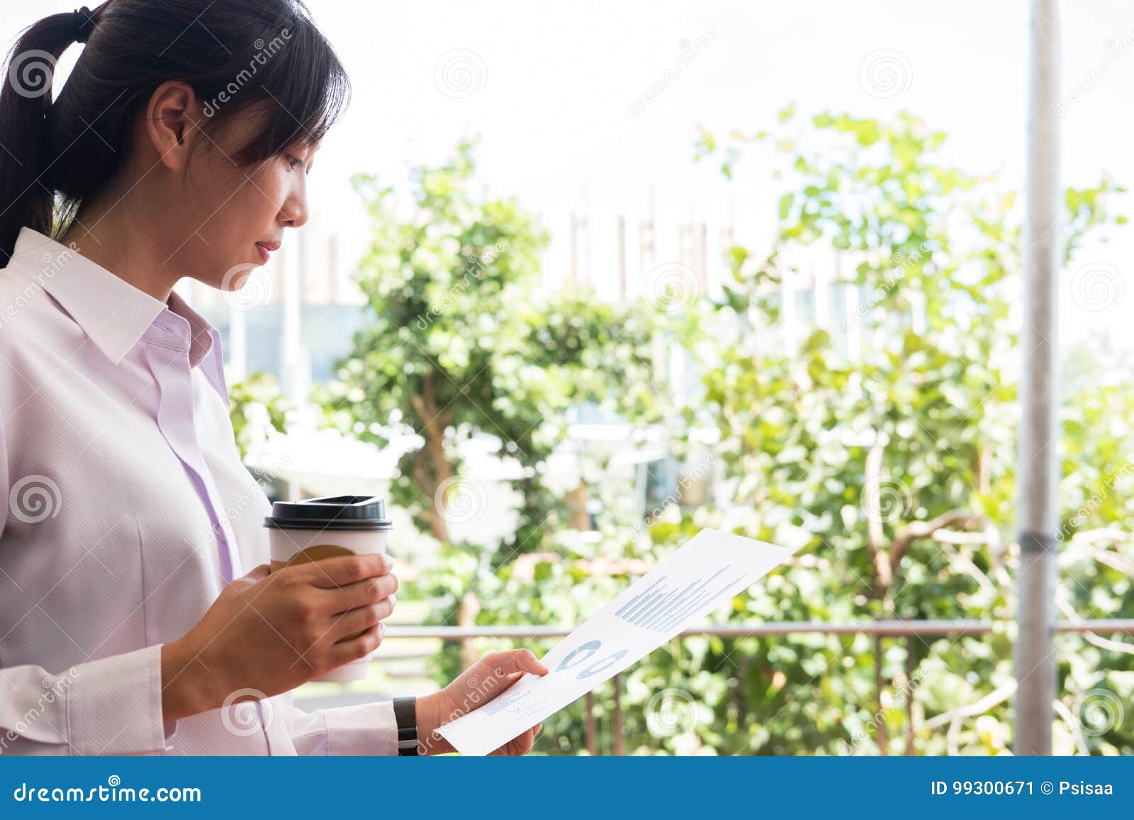 Outsi del grafico della tazza di caffè della tenuta della donna di affari & del riassunto finanziario. Grafico della bella della donna di affari della tenuta tazza di caffè & del riassunto finanziario fuori dell'edificio per uffici bella giovane donna asiatica con tè che analizza i grafici di investimento all'aperto gente di affari con la tazza di carta eliminabile che controlla i dati di vendita