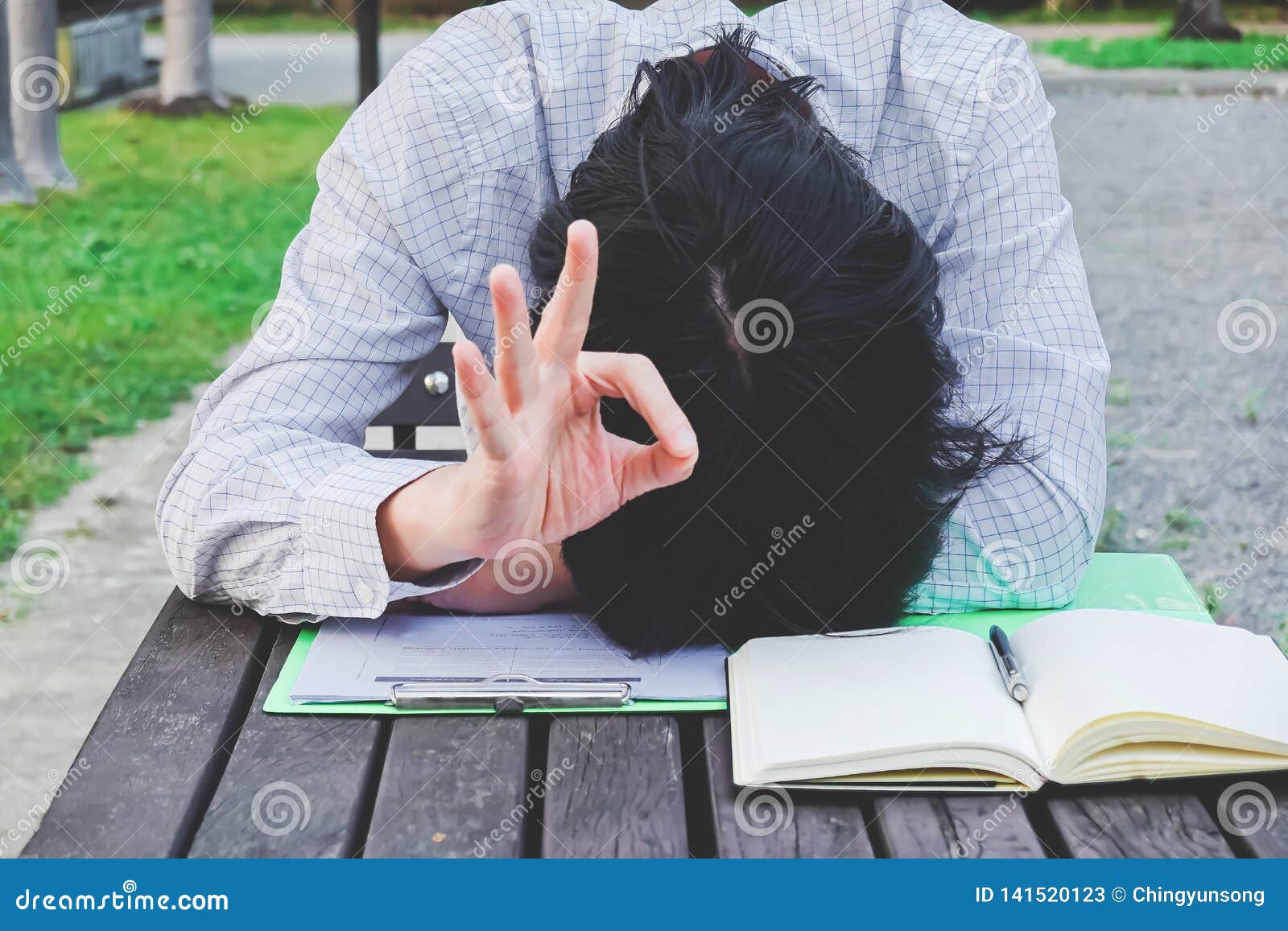 over-worked, tired businessman at office sleeping at his desk working over a book after he work all day but his showing ok gesture