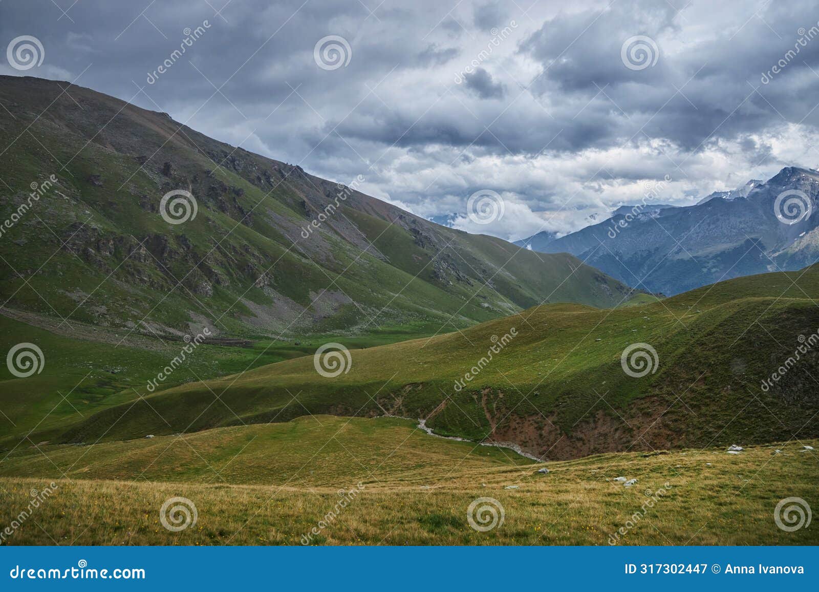 overcast skies loom above verdant mountain slopes with a winding path visible in the valley