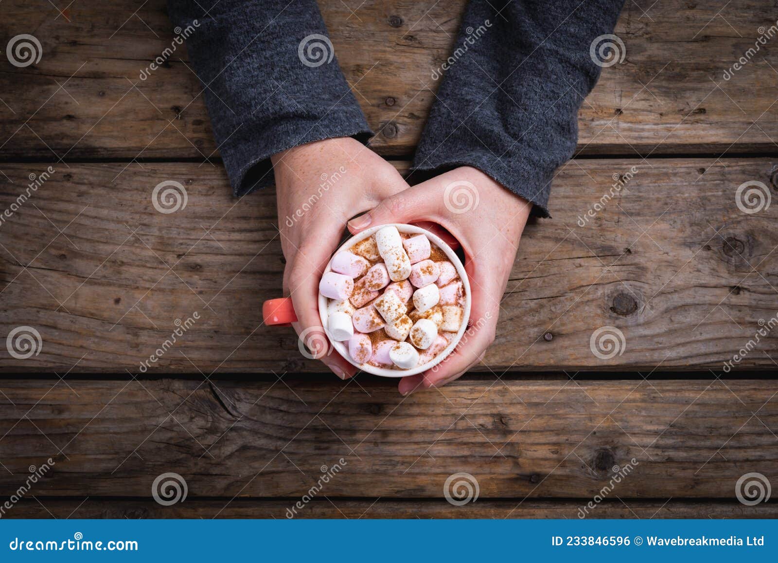 overhead view of female hands holding mug of hot chocolate drink filled with marshmallows at table