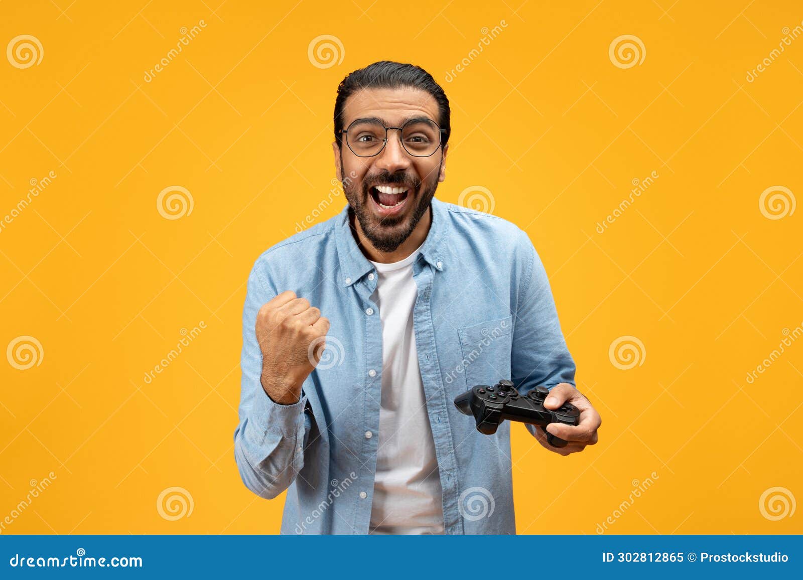 an overjoyed man with a beard and glasses holding a game controller clenches his fist