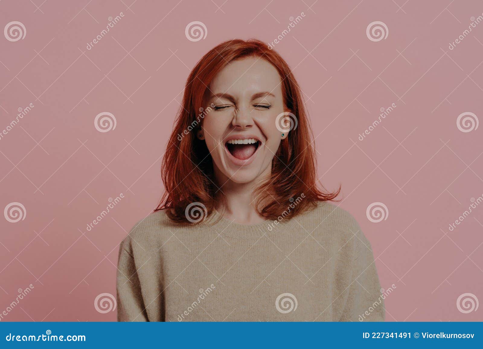 overjoyed red-haired woman laughing positively, with closed eyes,  on pink background