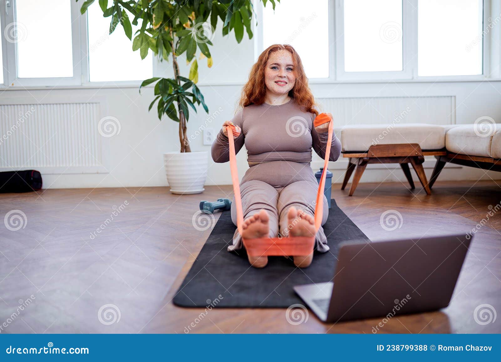 Overweight Redhead Female Doing Exercises For Legs Using Fitness Rubber