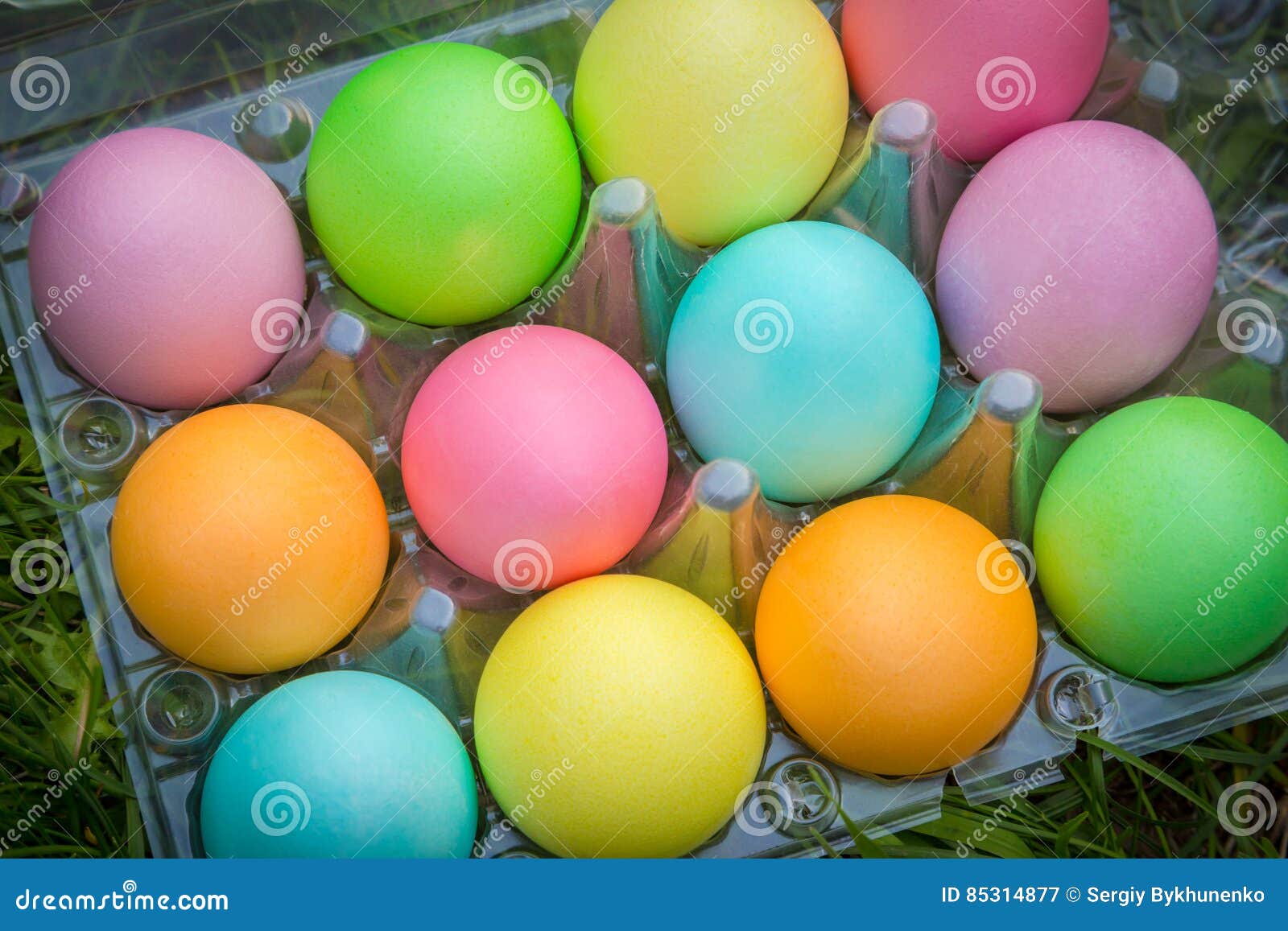 Muitos ovos da páscoa coloridos na bandeja plástica velha na grama verde