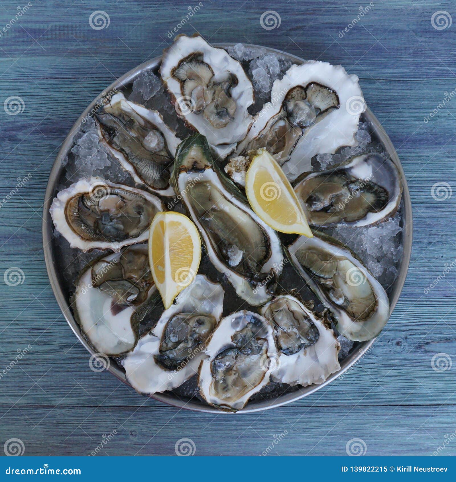 Fresh oysters with ice and lemons on tray on wooden flatlay